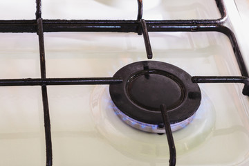 On the white gas stove the burner is lit from which the flame of natural gas is visible.