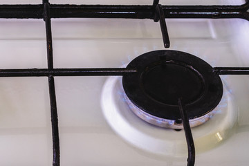On the white gas stove the burner is lit from which the flame of natural gas is visible.