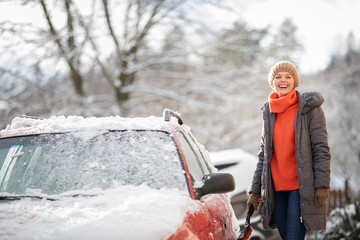 Pretty, young woman cleaning her car from snow after heavy snowstorm (color toned image)