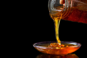 Golden liquid Organic Honey pouring from jar on black bacgrond