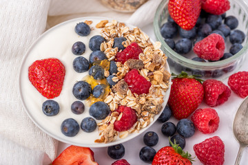 White yogurt in bowl with oatmeal and strawberries, blueberries and raspberries on the top on white background
