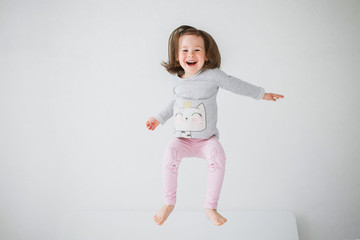 Cheerful girl jumping on the bed. The girl laughs and jumps. On a white bed, the girl is having fun...