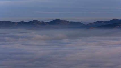 Landscape with inverse cloudiness and protruding peaks of mountains during sunrise.