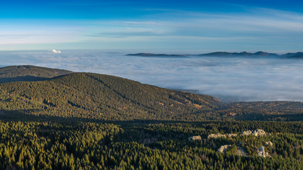 Landscape with inverse cloudiness and protruding peaks of mountains during sunrise.