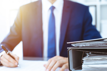 Binders with papers waiting to be processed with businessman or bookkeeper back in blur. Accounting...
