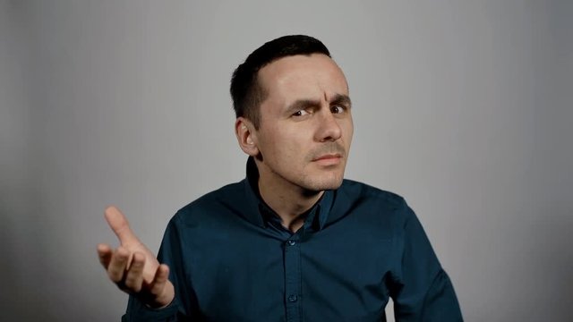 Closeup portrait of young business man gestures contemptuously to the interlocutor that he does not hear him in front of camera on white background. Charismatic actor play concept of emotions