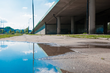 WARSAW - MAY 19: Town's big water puddles after rainy days, close up on May 19, 2019 in Warsaw, Poland. Puddle in focus with bridge and green scenery in the background, view from the surface