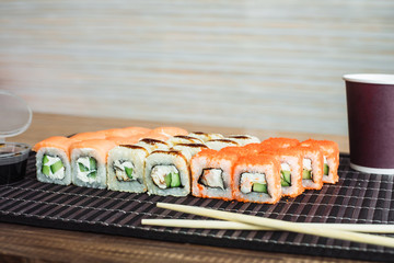 set of rolls from California and Philadelphia in the background of a cafe. Delicious European rolls with a glass of coffee. Tea in a disposable paper cup
