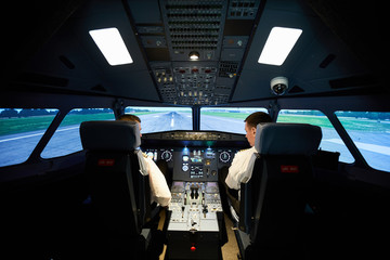 Rear view of serious male aviators in uniform sitting in armchairs and looking at radar displays while checking airplane before flight