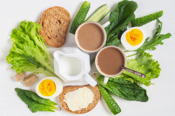 Healthy breakfast. Two cups of white coffee, eggs, toast with butter and leaves of spinach
