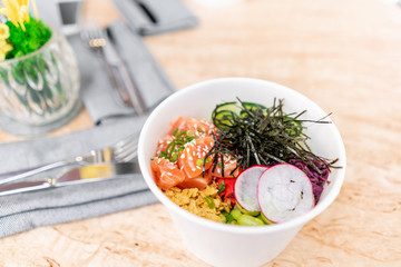 Traditional Hawaiian dish poke bowl with fork. Hawaiian salmon fish with rice, radish,cucumber, tomato, sesame seeds and seaweeds. Diet and Useful fast food
