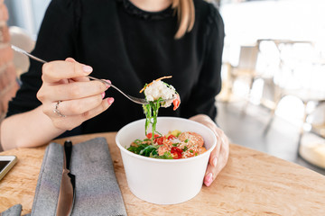 Woman eating traditional Hawaiian dish poke bowl with fork. Shrimps with rice, radish,cucumber,...