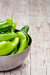 Fresh green raw peppers in metal bowl on rustic wooden table background.