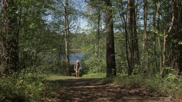 The young man goes to the camera from the shore of a forest lake. Tourism on forest lakes. 4K