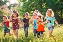 Large group of kids, friends boys and girls running in the park on sunny summer day in casual clothes .