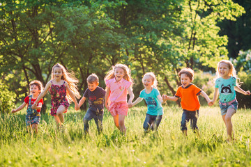 Obraz premium Large group of kids, friends boys and girls running in the park on sunny summer day in casual clothes .