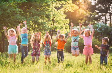 Group of friends running happily together in the grass and jumping. - obrazy, fototapety, plakaty