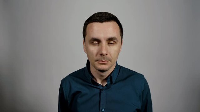 Closeup portrait of a young business man wants to sleep and starts falling asleep in front of a camera on a white background. Charismatic actor play concept of emotions