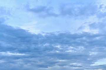 Blue sky with blue clouds. Above, above the clouds, a bright cloudless zone in the center. Below the clouds are stretched horizontally, crowded closely. At the very top a little light cloudiness.