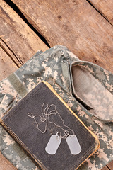 In memory of a brave soldier. Military camouflage clothes, old book, and dog tags on wood.