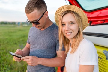 Young couple sitting in the trunk of a car on a summer day closeup. The guy with the phone in his hands looking at the screen
