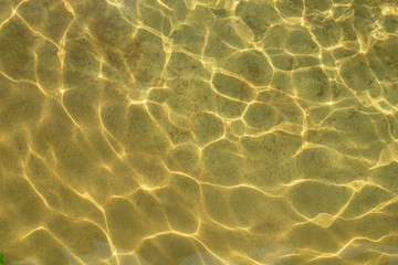 Clear sea water and sandy bottom background. Sand through the transparent water texture