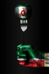 A hand with a drawn Chechnya flag holds a fork, on which is a ball with a drawn Ingushetia flag, a...