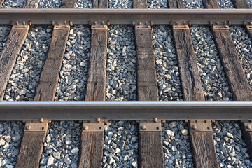 Steel railroad tracks cross wooden ties, and are set on top of a stone ballast surface, during a late afternoon day.