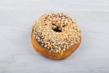 Chocolate donut sprinkled with nuts on white wooden background