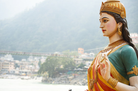 Close-up view of the statue of sitting Goddess Parvati on the riverbank of the Ganges river. Blurred Lakshman Jhula bridge in the background. Rishikesh, Uttarakhand, India.