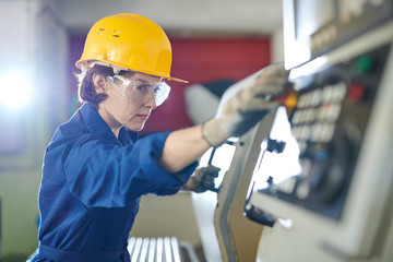 Side view portrait of female worker pushing STOP button while operating machine units at metal...