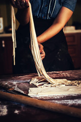 Young house wife preparing the homemade pasta at kitchen. Woman's hands holding long dough stripe for cooking pasta.
