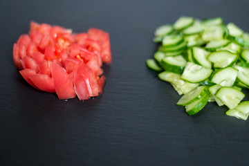 Sliced fresh cucumbers and tomatoes on a black background. Cooking salad from vegetables. The concept of healthy eating, vegetarianism.