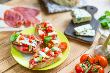 Traditional Italian bruschetta with blue cheese, feta, tomatoes, basil leaves, jamon on a wooden background.