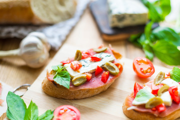 Traditional Italian bruschetta with blue cheese, feta, tomatoes, basil leaves, jamon on a wooden background.