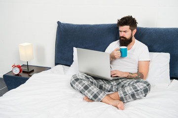Just woke up and already at work. Hipster bearded guy pajamas freelance worker. Remote work concept. Social networks internet addiction. Online shopping. Man surfing internet or work online