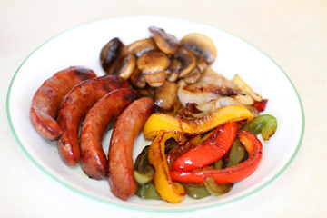 Plate of sausage with grilled bell peppers, mushrooms, and onion.