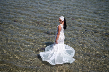 Wedding abroad. Wedding ceremony seashore. Bride white wedding dress stand in sea water. Wet...