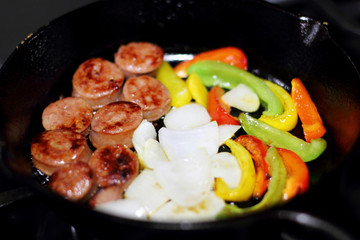 Sausage cooking on the stove in a cast iron skillet with bell peppers and onion.