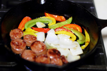 Sausage cooking on the stove in a cast iron skillet with bell peppers and onion.