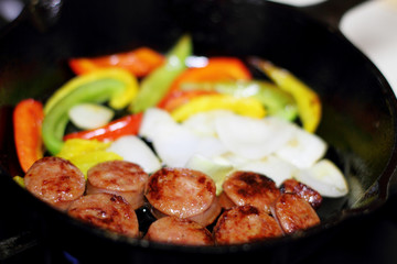 Sausage cooking on the stove in a cast iron skillet with bell peppers and onion.