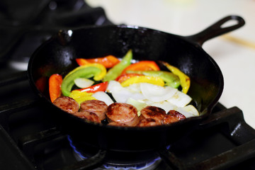 Sausage cooking on the stove in a cast iron skillet with bell peppers and onion.