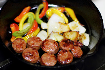 Sausage cooking on the stove in a cast iron skillet with bell peppers and onion.