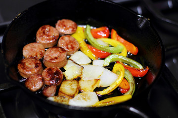 Sausage cooking on the stove in a cast iron skillet with bell peppers and onion.