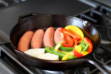 Sausage cooking on the stove in a cast iron skillet with bell peppers and onion.