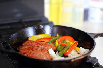 Sausage cooking on the stove in a cast iron skillet with bell peppers and onion.
