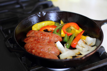 Sausage cooking on the stove in a cast iron skillet with bell peppers and onion.