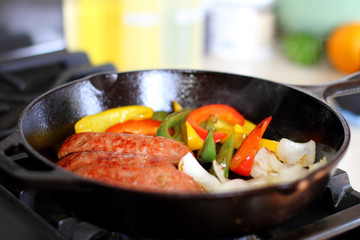 Sausage cooking on the stove in a cast iron skillet with bell peppers and onion.