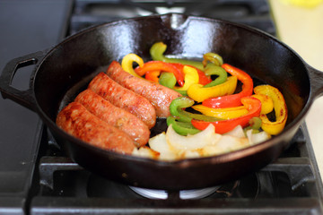 Sausage cooking on the stove in a cast iron skillet with bell peppers and onion.