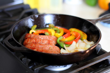 Sausage cooking on the stove in a cast iron skillet with bell peppers and onion.